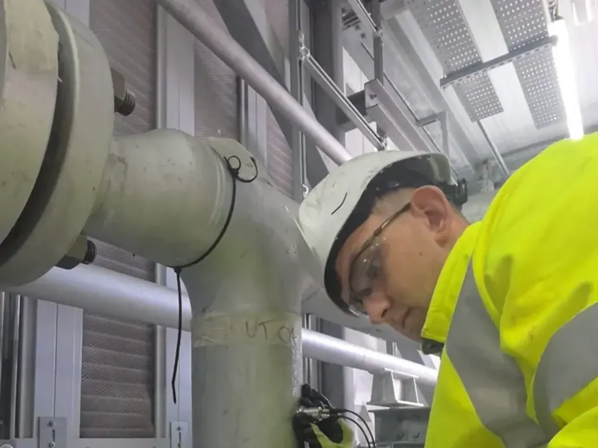Technician carrying out ultrasonic testing on a pipe tee with a handheld flaw detector